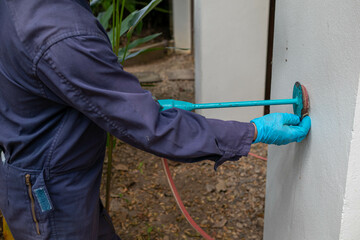 exterminate termite control company employee is using a termite sprayer at customer's house and searching for termite nests to eliminate. exterminate control worker spraying chemical insect repellant