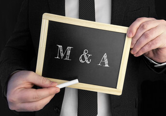 A businessman holds up a chalkboard with text Mergers and Acquisitions