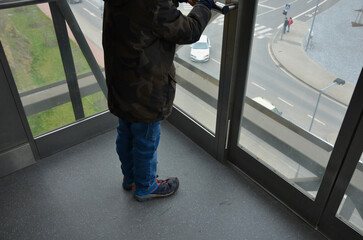 riding an outdoor elevator with glass walls can be stressful for people who suffer from vertigo from heights. the boy is holding on to the pipe handrail