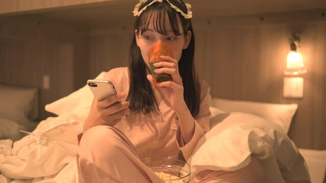 寝室でスマートフォンを使うパジャマ姿の女性