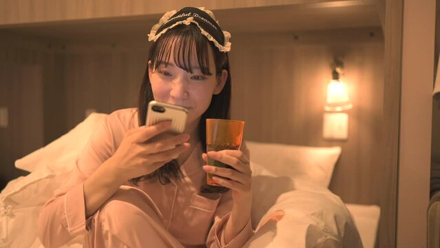 寝室でスマートフォンを使うパジャマ姿の女性