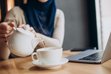 Modern muslim woman drinking tea and working on computer in a cafe