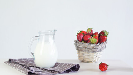 Lactose-free milk in a glass jug and strawberries in a wicker basket