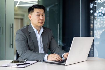 Surprised asian man looking at camera, mature adult boss businessman working inside office with...