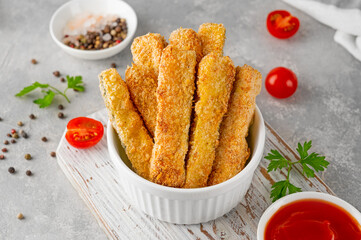 Baked crispy garlic parmesan zucchini sticks served with tomatoes sauce on a gray concrete background. Vegetarian healthy dish. Selective focus.