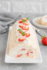Meringue roll Pavlova cake with cream and fresh strawberries on top on a gray background. Copy space