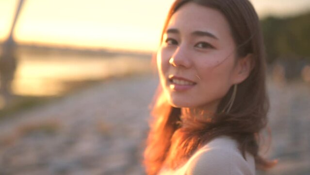 川辺で夕焼けの空を眺める女性の横顔アップ