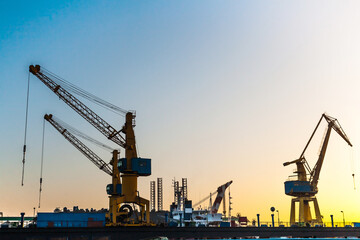 Fototapeta premium Silhouettes of harbor cranes at sunset. Shipyard at sunset.