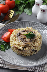 Bulgur garnish with champignons served with tomatoes on gray plate