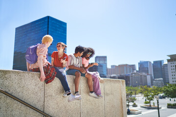 Young friends hanging out on ledge in sunny city