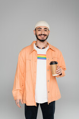 Smiling homosexual man with lgbt flag on t-shirt holding coffee to go isolated on grey.