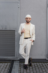 Well dressed gay man posing and looking at camera near building outdoors.