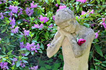 Der Trauernde (Steinfigur) mit Blume vor Rhododendronstrauch