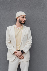 Well dressed gay man in beige suit and hat standing near wall outdoors.