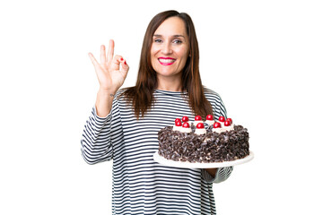 Middle age caucasian woman holding birthday cake over isolated chroma key background showing ok sign with fingers