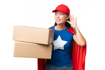 Super Hero delivery Asian woman holding boxes over isolated background listening to something by putting hand on the ear