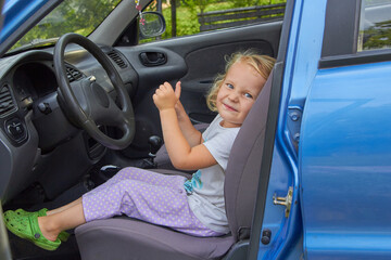 the girl sits in the car in the driver's seat,the girl is happy sitting in her father's blue car in the summer