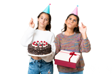 Friends girls holding gift and a birthday cake over isolated chroma key background with fingers crossing and wishing the best