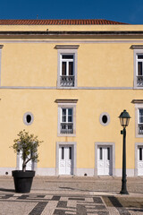 Fototapeta na wymiar Yelloe traditional portugese house with the blue sky, a plant, a street lantern and white windows
