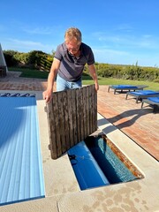 Man replacing the decking which hides the roller for a hidden slatted automatic pool cover