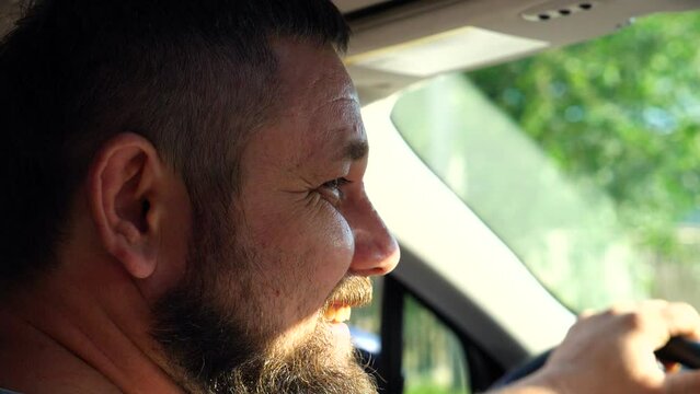 Profile of male driver riding by car. Face of man looking to passenger with smile. Happy bearded guy holding the steering wheel of his car during journey. Concept of family trip. Slow motion Close up