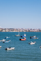 Fototapeta na wymiar Group of colored boats in the blue waters of the coast of Cascais, Portugal with the city on the horizon