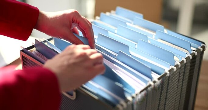 The hands of a business woman sort through documents in a box, close-up. Organization of information on the topic