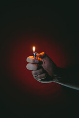 Hand of a young man with a cylindrical lighter on a red background.