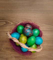 Multicolored painted Easter eggs in a basket on a wooden background, top view - 594997310