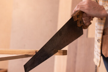 Crop male carpenter cutting wooden detail with saw while standing at workbench and working in joinery workshop