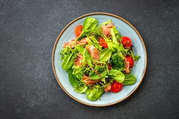 Green salad with fresh leaves, tomatoes and jamon at black table. Top view with copy space.
