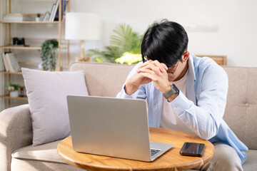 Focused concentrated young asian businessman sit at sofa with laptop, serious  male professional analyst working online on computer data watch webinar thinking of problem solution.