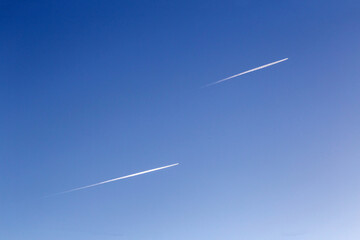 Dos aviones volando en paralelo en un cielo azul, dejando estelas blancas a su paso.