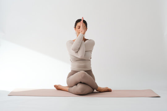Woman sitting on mat while practicing cow face pose in studio