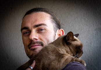 Portrait of a young man holding a Burmese cat