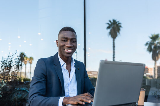 Cheerful black businessman working on laptop in outdoor cafe