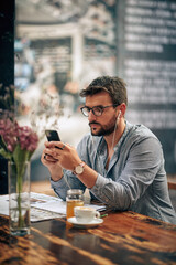 Businessman at cafe using smartphone with earphones, on a coffee break.
