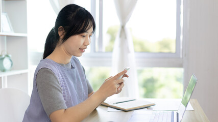 Asian woman having fun playing games on mobile phone, Play games on the sofa in the living room on weekends, Resting at home, Comfort zone, Touch screen mobile phone.