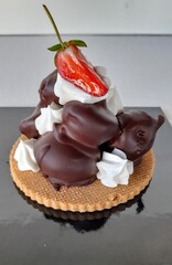 Profiterole typical French dessert made with a cream puff filled with custard, chantilly, cream or ice cream and covered with a chocolate cream and a decorative strawberry