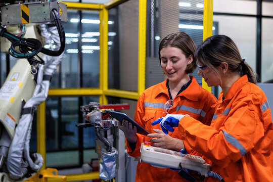 Girl engineer commissioning operating programming and looking at robot machine in the factory