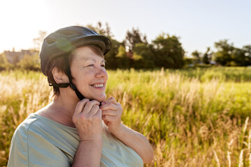 Senior adult plus size smiling woman wearing helmet standing with bicycle outdoors at nature....