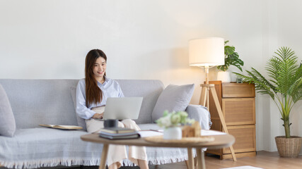 Woman using laptop to work or do homework at home with smiling face in her living room, Creating happiness at work with a smile, Live performance or video call with laptop, Work from home.