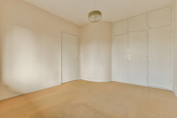 an empty room with white cupboards and closets on the wall to the right, there is a lamp hanging light in the