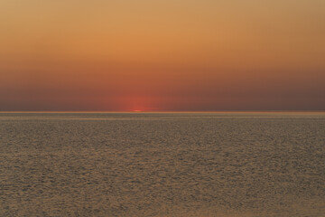 Obraz premium Sunset on the coast. The sun set below the horizon. Orange sky. Ripples on the water from the wind. Space for text. Natural background.