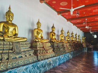 Row of statues of the Buddha illuminated by light shining through a red ceiling