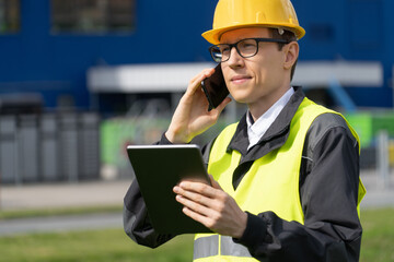 Engineer with phone and digital tablet on a background of logistic center