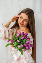 Portrait of sexy beautiful young woman with long hair. Model with a bouquet of lilac tulips on white. Spring. Holidays.