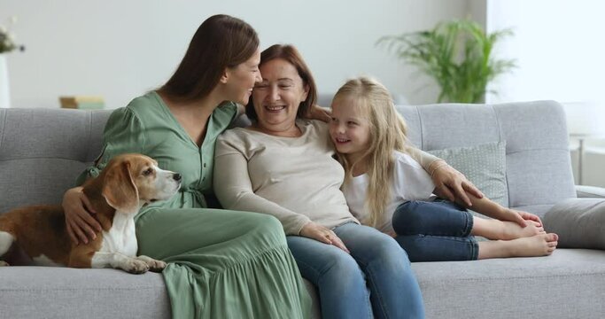 Smiling three generations of women, multi-generational family with dog sit on sofa, spend free time together on weekend at home, having fun, show love, ties, support, enjoy bond and warm relationship