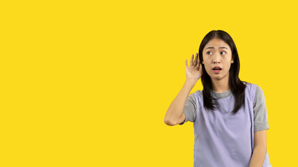 Asian woman eavesdropping or overhearing secret conversation isolated on yellow background, Gossip,...