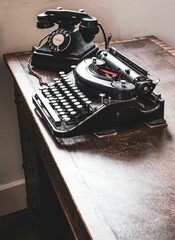 Antique typewriter and rotary phone against a backdrop of a bright window